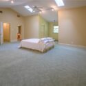 A bedroom with grey carpeting and a white bed